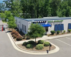 Midgard Self Storage building with blue accents, gated entrance, and landscaped shrubs under clear blue sky.