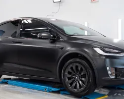 Matte black Tesla Model X SUV in a bright garage on a blue vehicle lift with polished concrete floors.