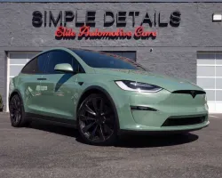 Green Tesla Model X parked in front of Simple Details automotive care center with black rims and clear skies.