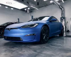 Matte blue Tesla Model S parked inside a modern garage with polished concrete floor and industrial lighting.