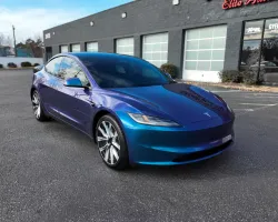 Sleek blue Tesla Model S parked in front of a gray building with large glass windows under a clear sky.