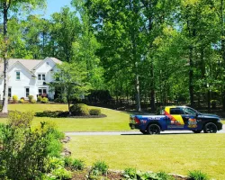 Colorful service truck parked on driveway outside large white house surrounded by green trees and lawn