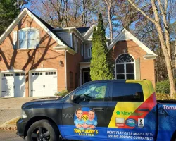 Tom and Jerry's Roofing branded truck parked in front of a brick house with white garage doors on a sunny day.
