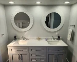 Modern bathroom with dual sinks, round mirrors, and white countertop under recessed lighting.