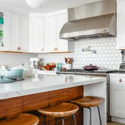 Modern kitchen with white cabinetry, hexagonal tile backsplash, wooden stools, and stainless steel appliances