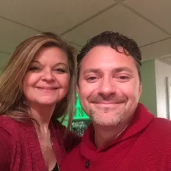 Smiling man and woman wearing red sweaters taking a selfie indoors with a green-lit background.