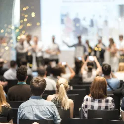 a group of people sitting in a room with a stage and a crowd