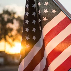 Close-up of an American flag waving with sunlight shining through at sunset.