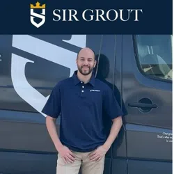 Smiling man in navy polo and beige pants stands next to a black vehicle with Sir Grout logo and crest.