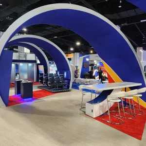 Modern conference booth with blue and white arches, seating areas, and a vibrant carpeted floor at trade show.