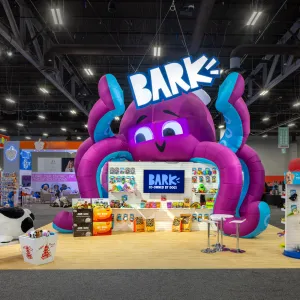 Colorful trade show booth with giant inflatable purple octopus and Bark dog product displays.