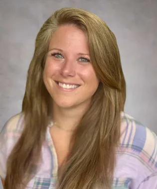 Smiling woman with long blonde hair wearing a plaid shirt against a gray background.