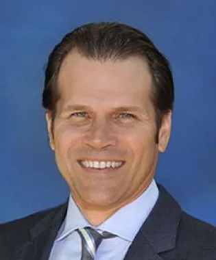 a man wearing a suit and tie smiling at the camera.