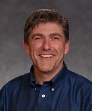 a man wearing a blue shirt and smiling at the camera.