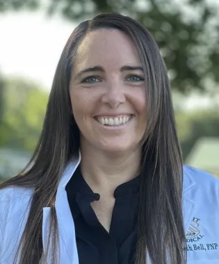 Smiling female medical professional wearing white coat and black shirt with long straight hair outdoors..