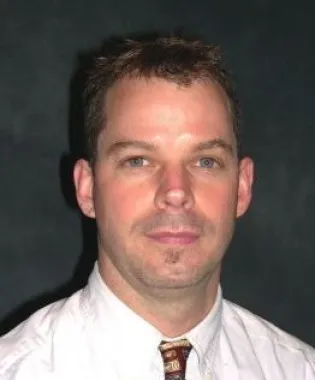 a man wearing a suit and tie smiling at the camera.