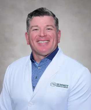 Smiling male doctor wearing a white coat with Summit Medical Group logo on a neutral background.