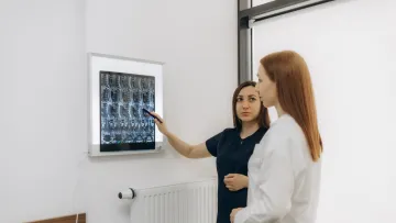 Medical professional explaining spinal X-ray images to a patient in a bright clinic room.