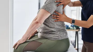 Physical therapist adjusting a patient's upper back during a therapy session in a bright clinical setting