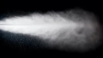 White mist or spray dispersing in the air against a black background, showing fine water droplets and vapor.