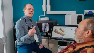Dental consultation with a patient and dentist reviewing images on computer screens.