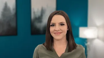 Smiling woman with straight brown hair in green medical scrubs standing against teal and white office background