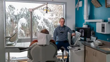 A dentist consults with a patient in a modern clinic with snowy outdoor views.