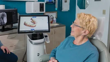 Older woman smiling in a dental office, looking at a digital display of teeth.