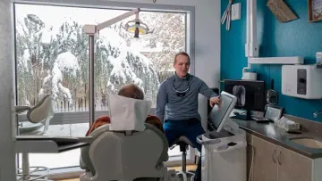 Dentist consulting with patient in a modern dental office with snowy outdoor view seen through large windows.