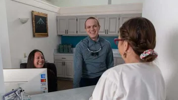 Dental office reception with receptionist, dentist, and patient smiling during check-in at front desk