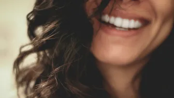 Close-up of a woman's smile with white teeth and curly dark hair, highlighting happiness and dental health.