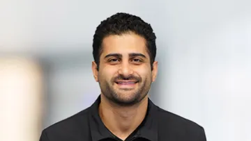 Smiling man in a black jacket with a blurred background for a professional look.