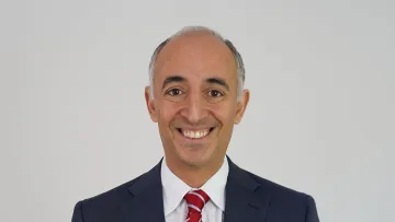 Professional man in a suit smiling against a plain background.