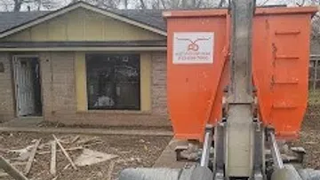 Orange concrete mixer machinery in front of a house under renovation with bare trees in background