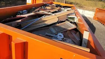 Orange dumpster filled with wood debris and construction waste outdoors on a sunny day.
