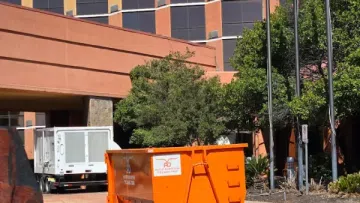 Bright orange dumpster container outside a multi-story office building on a sunny day