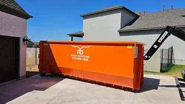 Large bright orange Austin Dumpsters container placed in a residential driveway on a sunny day.
