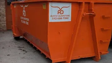 Large orange Austin Dumpsters container placed on a concrete driveway near a house with trees in the background.