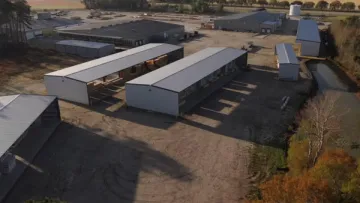 Aerial view of industrial buildings and warehouses surrounded by trees and open land on a sunny day.
