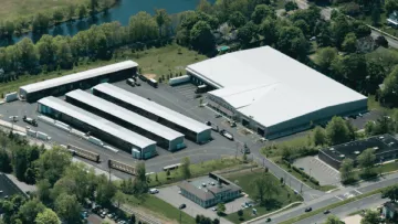 Aerial view of a large warehouse facility with multiple loading docks, trailers, and surrounding greenery.