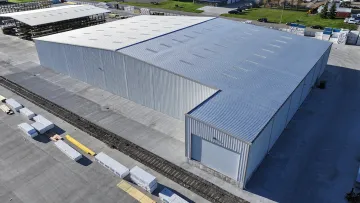Aerial view of a large industrial warehouse with metal roofing and concrete surroundings.