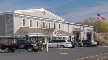 Commercial building with parking lot, multiple vehicles, an American flag, and clear blue sky in the background