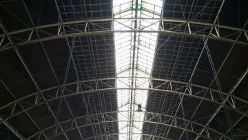 Interior view of a large industrial roof structure with metal beams and a central skylight.