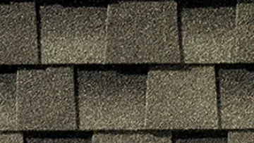 Modern house with gray asphalt shingle roof, stone accents, and a clean concrete driveway under a sunny sky
