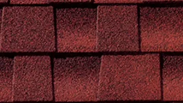 Modern house with beige walls and red composite shingle roof under blue sky, close-up of textured red shingles.
