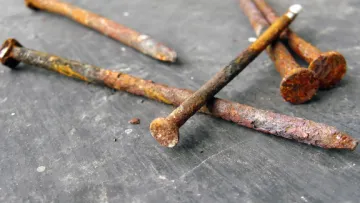 Close-up of rusty nails scattered on a dark textured surface showing corrosion and decay.