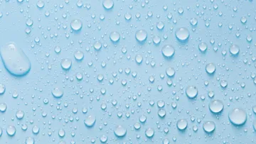 Close-up of clear water droplets on a smooth light blue surface with various sizes and reflections.