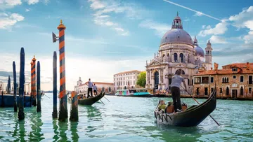 Gondolas floating on Venice canal with historic Basilica di Santa Maria della Salute under blue sky.