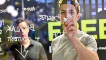 Two men brainstorming with notes on a transparent board in a modern office environment.
