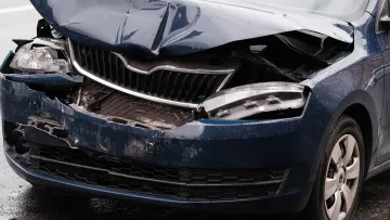 Blue car with severe front-end damage after a collision, showing crumpled hood and broken headlights.